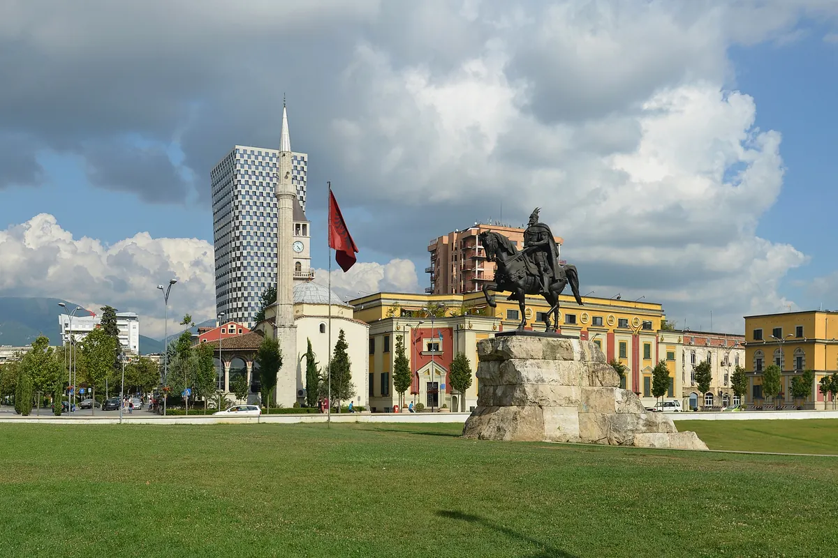 The bronze equestrian statue of Skanderbeg on a stone plinth, with the Et'hem Bey Mosque minaret and the clock tower rising behind trees